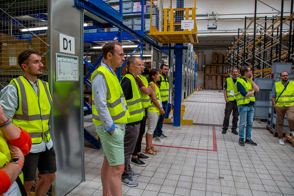 New hires in yellow safety vests stand in a warehouse, receiving employee training for peak season warehouse safety and order processing