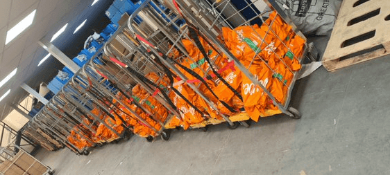 A staging area for outgoing ecommerce orders in a warehouse. Rolling carts are lined up in the staging area, filled with orange packages ready for parcel shipping.