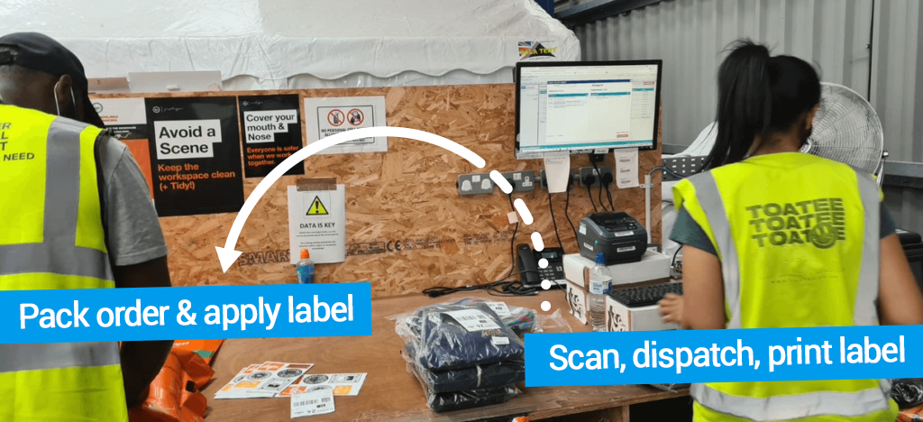 Workers in UK-based ecommerce brand Hype’s warehouse stand at a shipping station with products, computers, and shipping labels, working in pairs to pack and ship items during peak season. The person on the right scans, dispatches, and prints labels as the person on the left packs orders and applies shipping labels.
