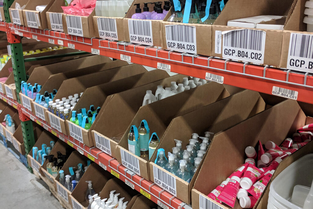 Ecommerce peak season inventory stored in barcoded bins on warehouse shelves; small bottles of lotion, hand sanitizer, and body care products ready to pick