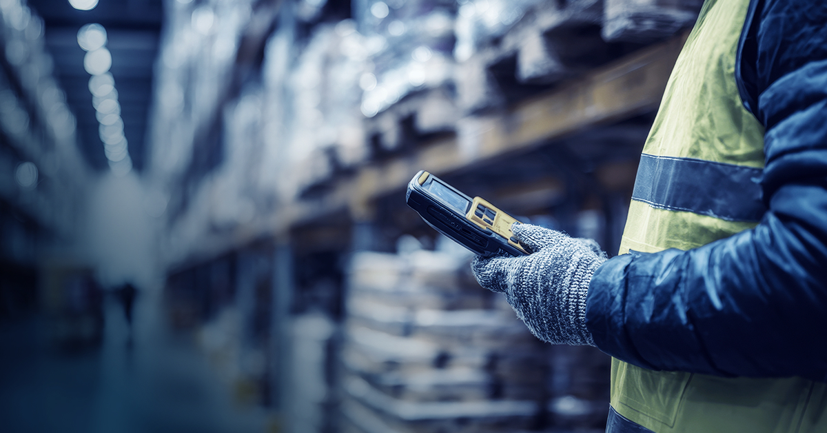 An image showing a warehouse worker holding a barcode scanning device while standing between a warehouse aisle.