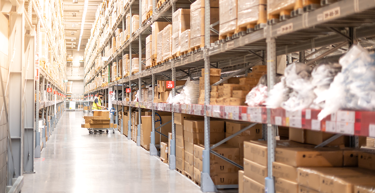 Large direct-to-consumer warehouse with parcels and pallets on metal warehouse shelves and a worker loading large parcels onto a trolley.